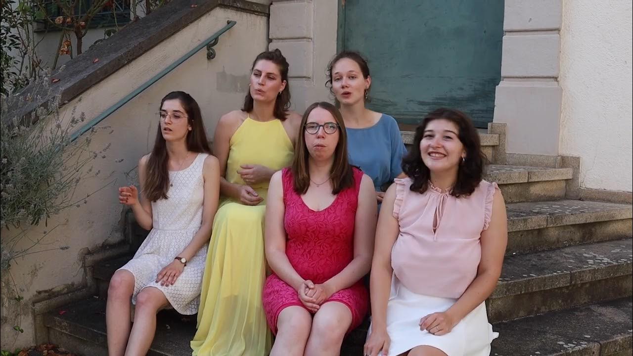 Embedded video: mata voices sit and sing in colorful dresses on steps in front of an old building